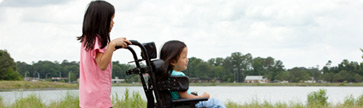 sisters, one pushing her sister's wheelchair through the park